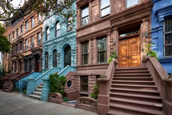 Colorful row of brownstone townhouses with stairs and entry doors along a New York City street.