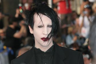 Marilyn Manson on the red carpet in a black suit with pale makeup and dark hair.