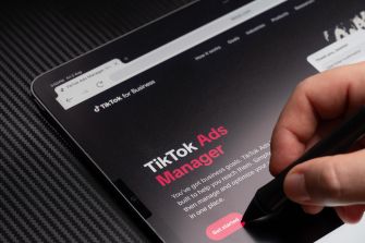 A hand using a stylus on a tablet screen displaying the TikTok Ads Manager interface.