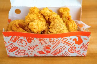 Crispy fried chicken pieces stacked in a Popeyes-branded takeout box on a wooden surface.