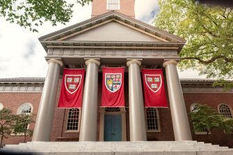 Entrance to a Harvard University building with tall columns and three red banners hanging between them.