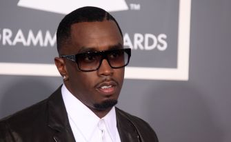 Sean Combs wearing dark sunglasses and a dark suit with a white shirt, posing on the Grammy Awards red carpet.