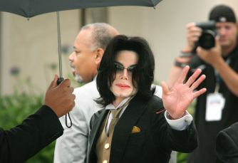 Michael Jackson, in a dark suit with a tan vest, waves to photographers during a public appearance.