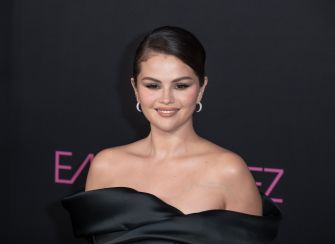 Selena Gomez on the red carpet wearing a black off-shoulder gown, smiling at the camera.