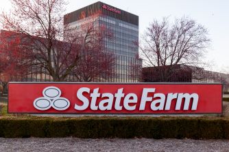 State Farm sign in front of a modern office building, with leafless trees and a trimmed hedge in the foreground.
