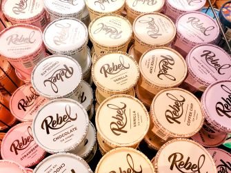 Assorted Rebel ice cream pint containers in pastel colors stacked together, each displaying the Rebel logo on the lid.