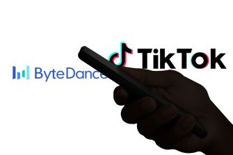 Hand holding a smartphone in front of ByteDance and TikTok logos.