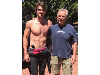 Conor Kennedy, son of Robert F. Kennedy Jr., stands outdoors shirtless beside an older man wearing a blue T-shirt.