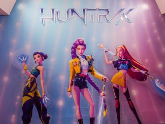 Three anime-inspired female characters in bright neon outfits pose together on a promotional backdrop.
