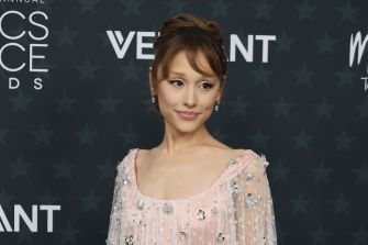 Ariana Grande stands on a red carpet in a pale pink, beaded gown with a sheer overlay.