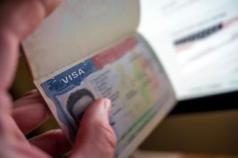 Close-up of a hand holding a passport and turning to reveal a visa page with a blue "VISA" stamp.