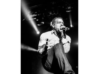 Robert Clivillés performing on stage, holding a microphone and singing under bright stage lights.