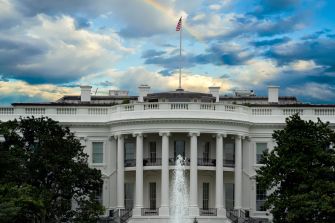 Front view of the White House with a fountain in the foreground, flanked by trees under a partly cloudy sky.