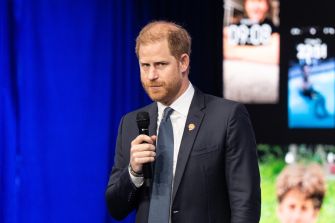 A man in a dark suit and tie speaks into a handheld microphone on stage.
