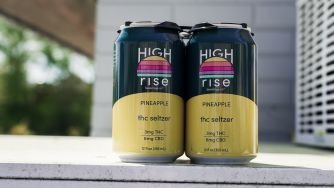 Two High Rise pineapple THC seltzer cans sit on a surface outdoors.