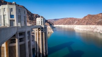 Concrete dam and spillway on a calm blue reservoir, with red canyon walls in the background.