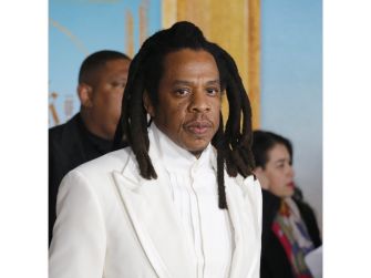 Shawn Carter (Jay-Z), with long dreadlocks and wearing a white suit, looks toward the camera.