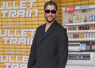 Benito Martínez Ocasio, known as Bad Bunny, stands in a black suit with sunglasses in front of a Bullet Train promotional backdrop.