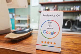 A small stand-up placard on a wooden counter reads "Review Us On Google" with the Google logo and five-star graphic, inviting customers to tap and leave a review.