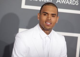 Chris Brown in a white suit poses for photographers on a red carpet at a Grammy Awards event.