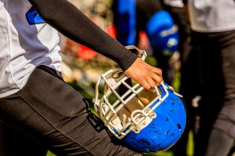 Close-up of a football player in a white jersey holding a blue helmet with a gold face mask during practice.