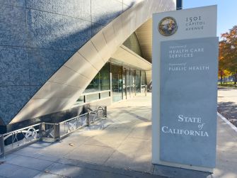 Exterior view of a California state government building with a tall rectangular sign displaying the State of California seal and the words Health Care Services and Public Health.