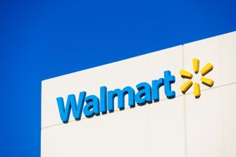 Walmart logo on the side of a white building with a clear blue sky behind.