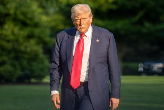 Donald Trump, former president of the United States, walking across a grassy lawn in a dark suit with a bright red tie.