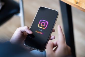 A hand holds a smartphone displaying the Instagram logo with the words "from Meta" on the screen.
