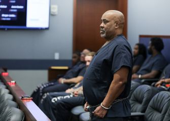 Duane "Keffe D" Davis stands in a Las Vegas courtroom wearing a blue jail uniform, with jurors and others seated in the background.