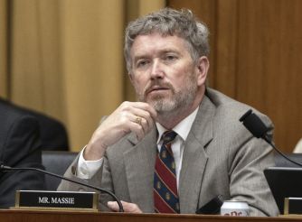 Thomas Massie, the Kentucky Republican U.S. representative, sits at a desk on the House floor wearing a light gray suit and striped tie, with his hand resting near his mouth.