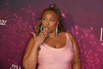 Lizzo in a pink sleeveless dress with large hoop earrings blows a kiss at a public event.