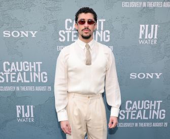 Bad Bunny (Benito Antonio Martínez Ocasio) posing on the red carpet in a cream-colored suit and sunglasses at the premiere of the film Caught Stealing.