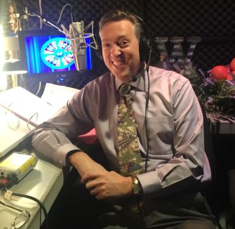 Jim Thornton smiles in a radio studio, wearing a headset and seated at a console with a microphone.