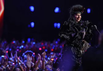 Lady Gaga performs onstage in a black outfit before a cheering, light-filled crowd.