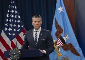 Pete Hegseth speaks at a podium between the U.S. and Defense Department flags.
