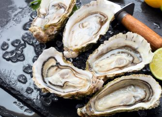 Raw oysters on ice with a shucking knife, lemon and lime wedges.