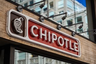 Chipotle restaurant sign mounted on a brick building beneath exterior lights.