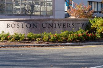 Boston University sign and landscaped campus entrance beside a roadway.