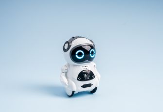 Small white AI robot toy with glowing blue eyes standing against a light blue background.