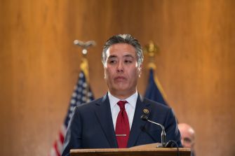 Rep. Mark Takano speaks at a podium with U.S. flags behind him.