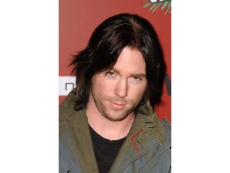 Elijah Blue Allman poses at an event wearing a dark shirt and olive-green jacket.