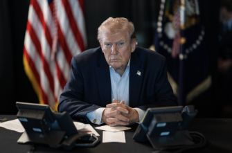 President Donald Trump sits at a table between U.S. and presidential flags.