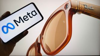 Meta logo displayed on a smartphone beside a pair of Ray-Ban smart glasses.