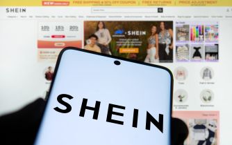Smartphone displaying the SHEIN logo in front of the retailer’s online marketplace webpage.