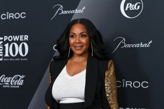 Erica Campbell poses on a red carpet in a black blazer with gold sequin sleeves.