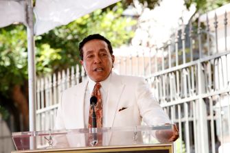 Smokey Robinson speaks at a podium outdoors.