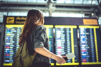 Traveler holding a boarding pass stands before airport departure screens.
