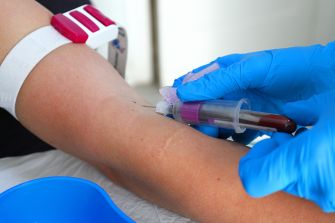 A gloved medical professional draws blood from a patient’s arm into a collection tube.