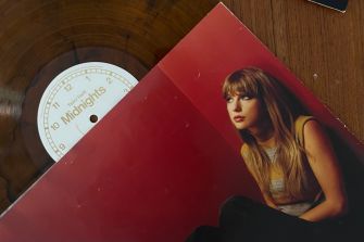 A Taylor Swift vinyl record and red album sleeve featuring her portrait lie on a wooden surface.